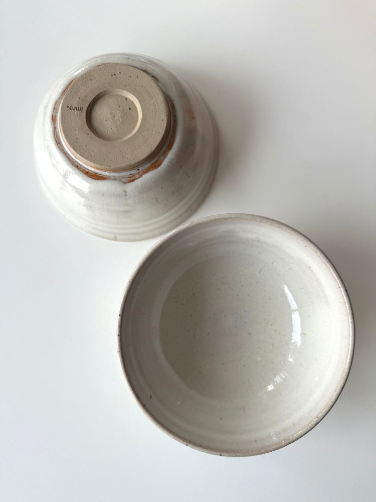 twee lichte handgemaakte kommen, een op zijn kop op een witte tafel