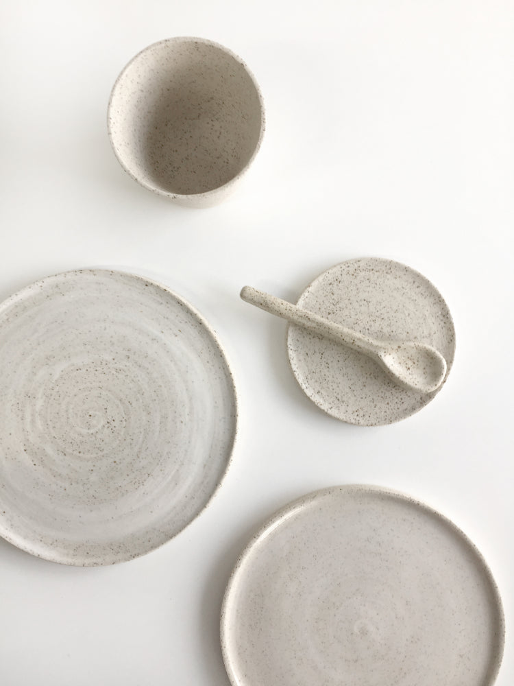 Verschillende handgemaakte gespikkelde cakeborden en een schotel van keramiek met bijpassend kopje en keramieken lepeltje