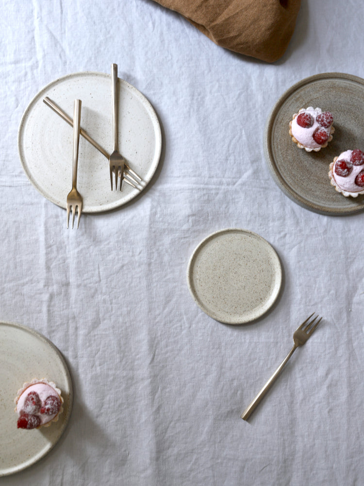Verschillende handgemaakte cakeborden en een schotel, bruine en wit gespikkelde, bij elkaar gefotografeerd op een tafelkleed met cake erop