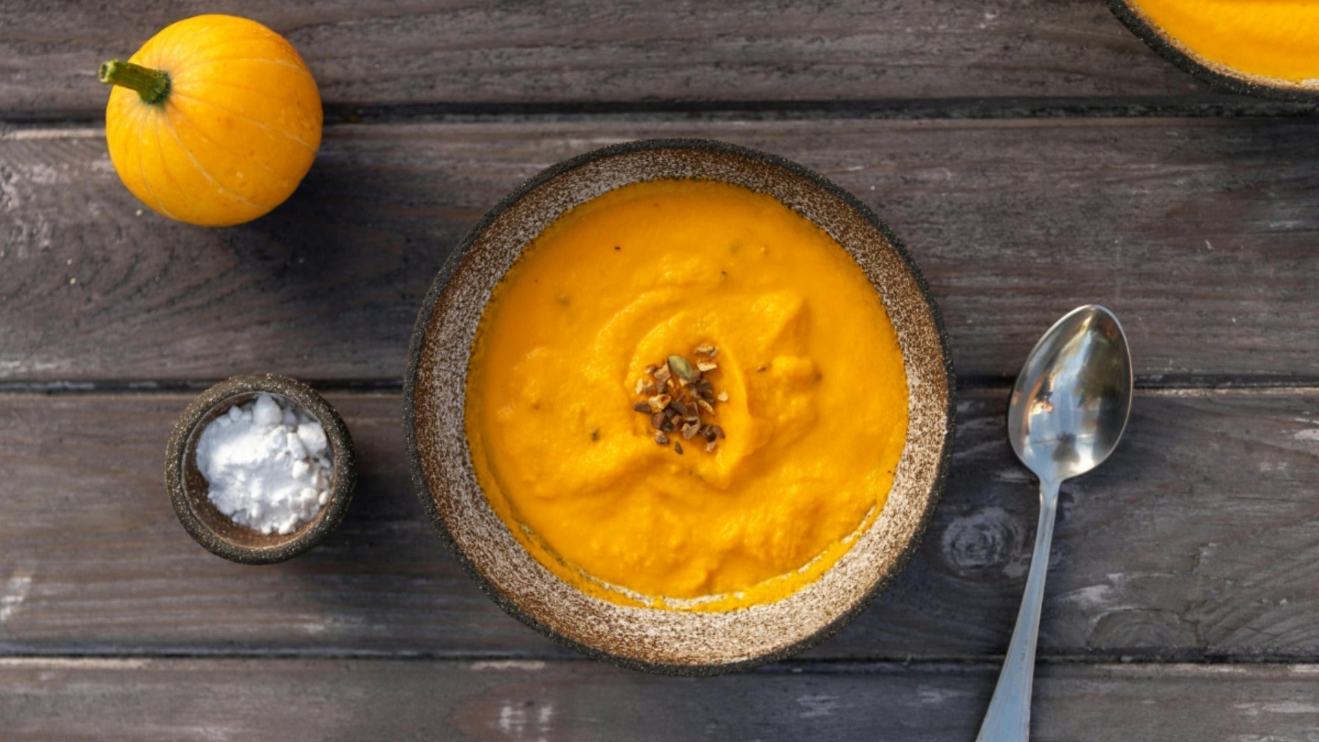 Handgemaakte keramiek kom met pompoensoep met lepel op een houten tafel, van bovenaf gefotografeerd