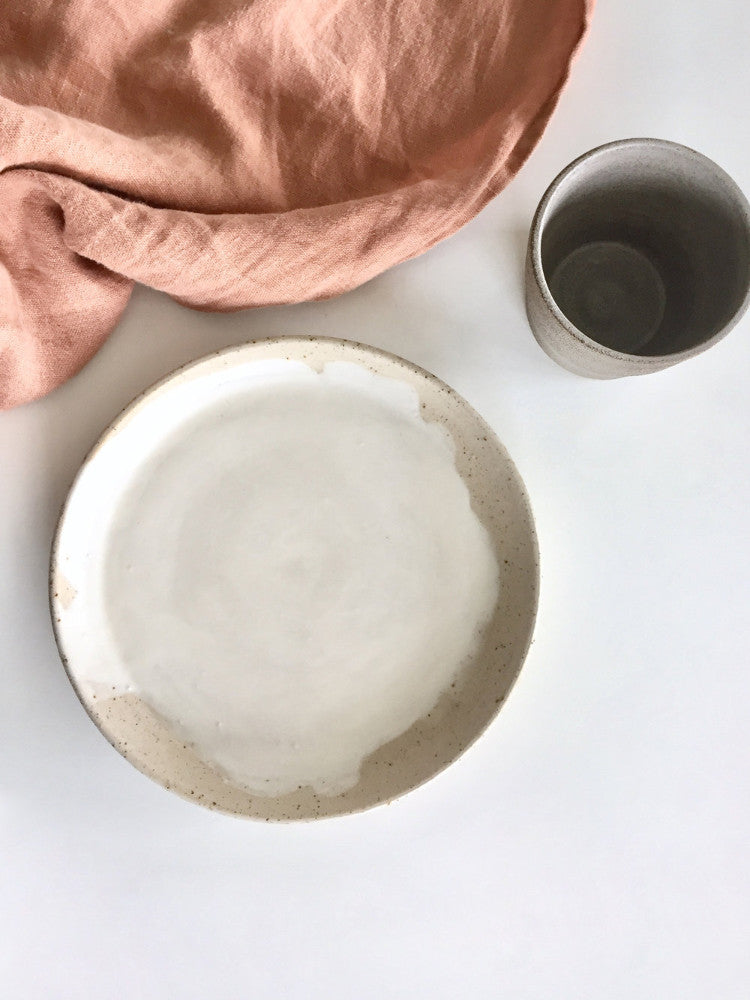 Handgemaakt keramiek bord en kopje met een theedoek ernaast, bovenaanzicht. Slowliving vibe