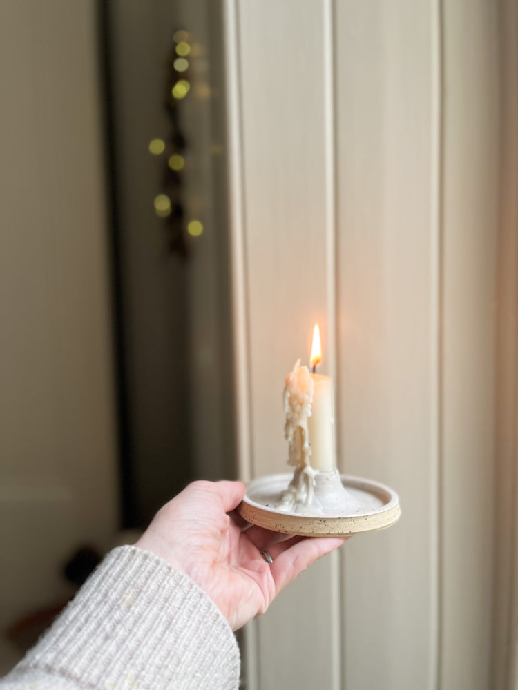 Handgemaakte kaarsenhouder van gespikkeld keramiek met een brandende kaars erin, die wordt vastgehouden door een hand.