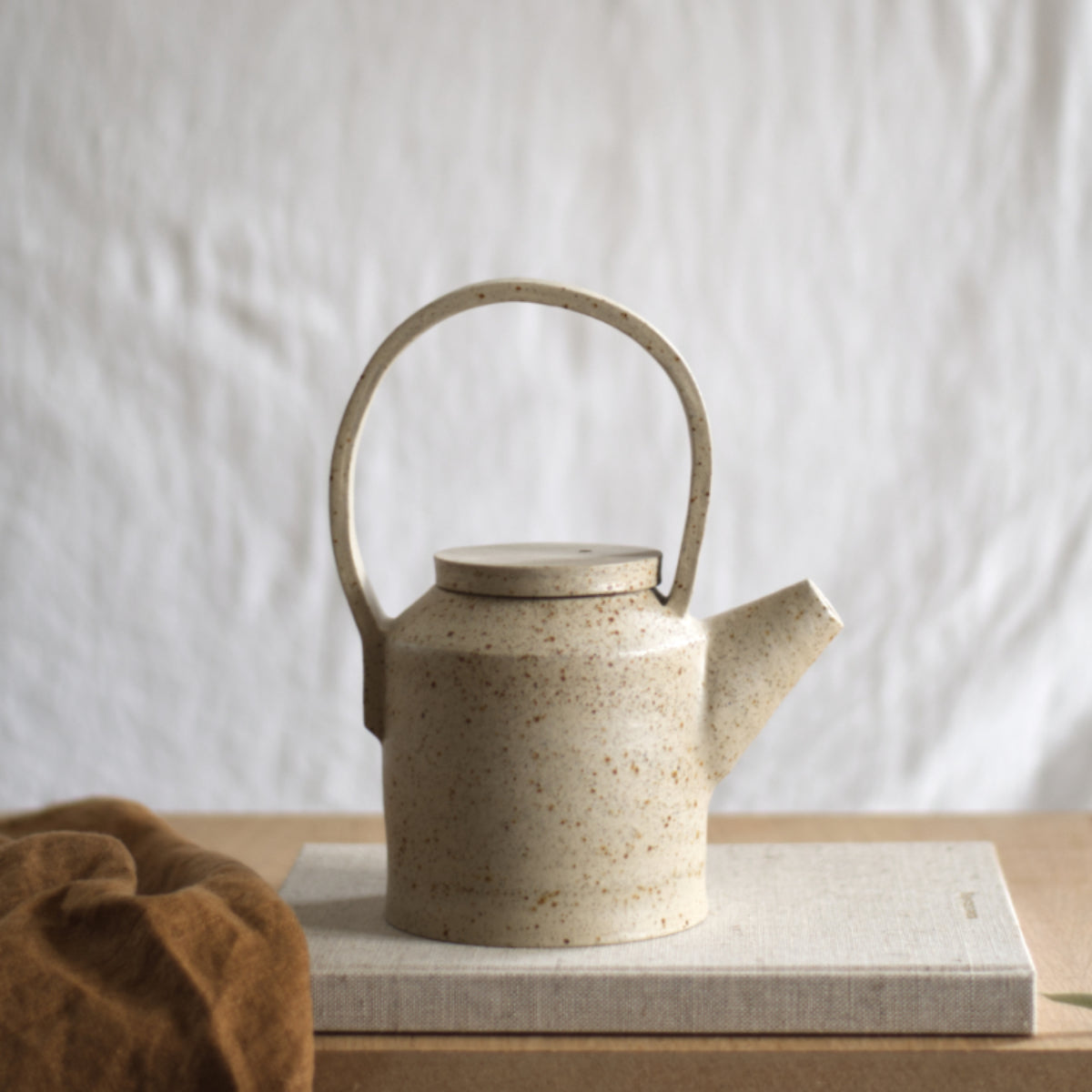 Handgemaakte kaarsenhouder van gespikkeld keramiek met een brandende kaars erin, die wordt vastgehouden door een hand.