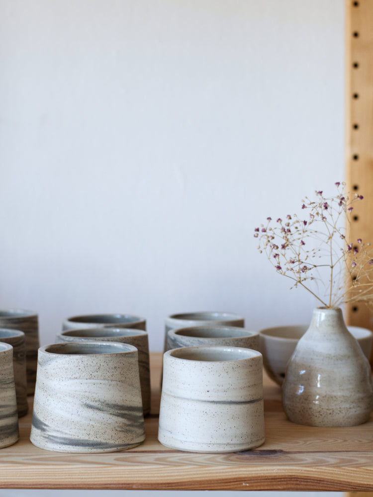Handgemaakte landschapskopjes, gedraaid van drie kleuren klei in rijen opgesteld, met een handgemaakt vaasje ernaast