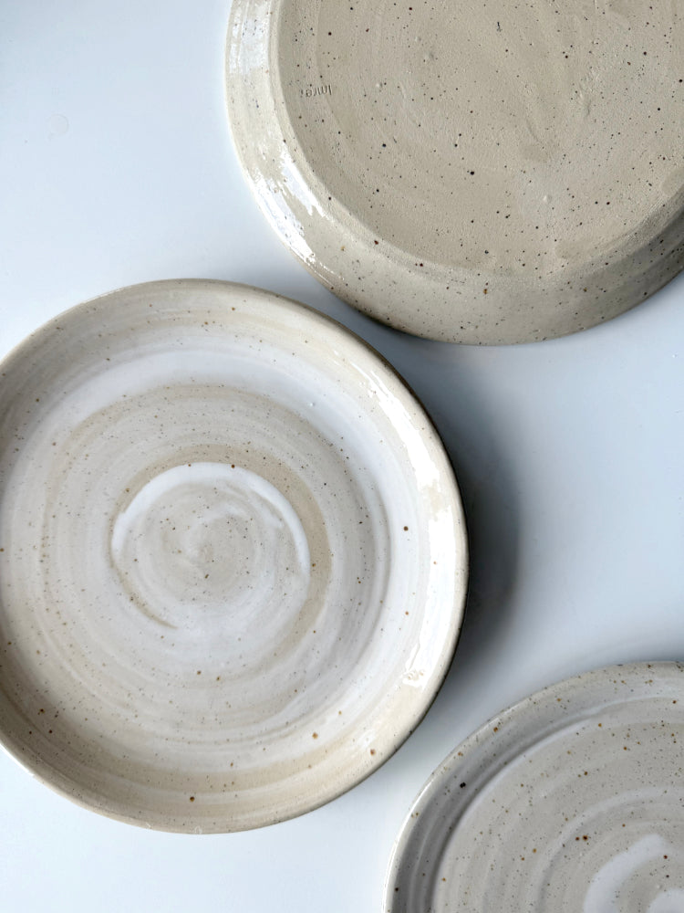 Handgemaakte lunchborden whitewashed  van gespikkeld steengoed met glanzend glazuur, een bord ligt op zijn kop