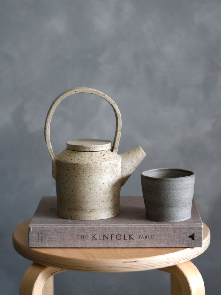 Bruin handgemaakt kopje naast een theepot op een boek op een kruk