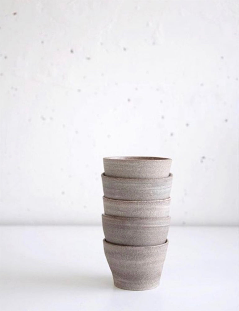 Bruin-grijze handgemaakte kopjes, opgestapeld. Afgebeeld tegen een witte muur