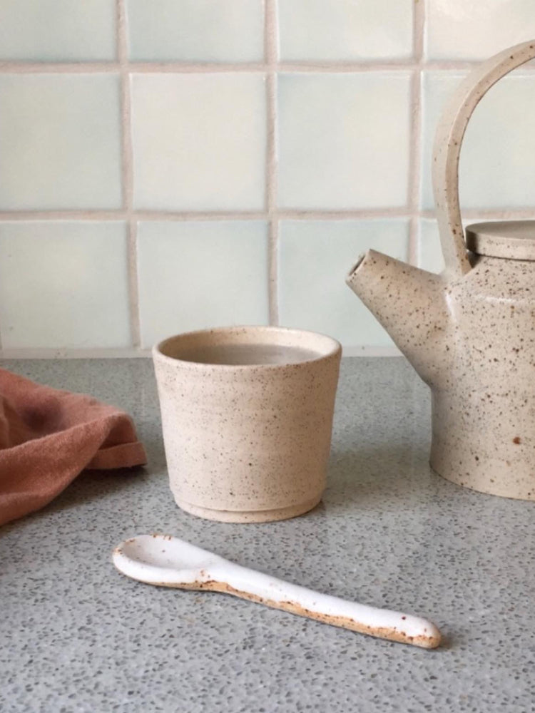 Handgemaakt licht keramieken kopje met een keramieken lepeltje en handgemaakte theepot