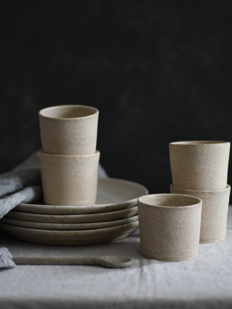 Handgemaakte kopjes en borden gestapeld op een tafelkleed met donkere achtergrond