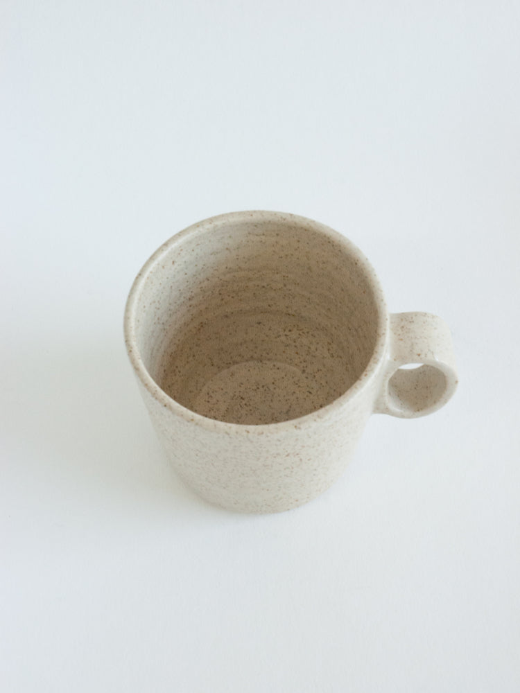 Handgemaakte lichtgespikkelde keramieken mok met zichtbare binnenzijde op witte achtergrond