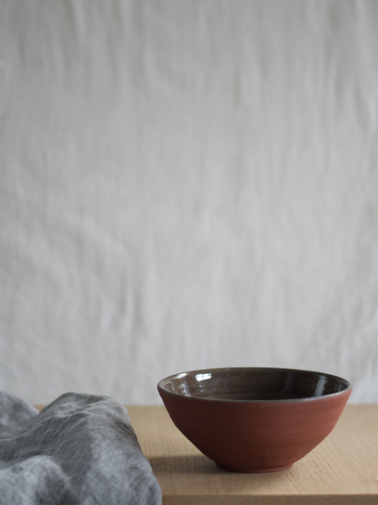 Handgemaakte rode keramieken kom op houten ondergrond met theedoek