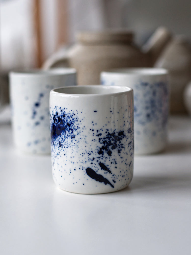 Handgemaakte witte porseleinen kopjes met blauwe spetters op een rijtje op een witte tafel