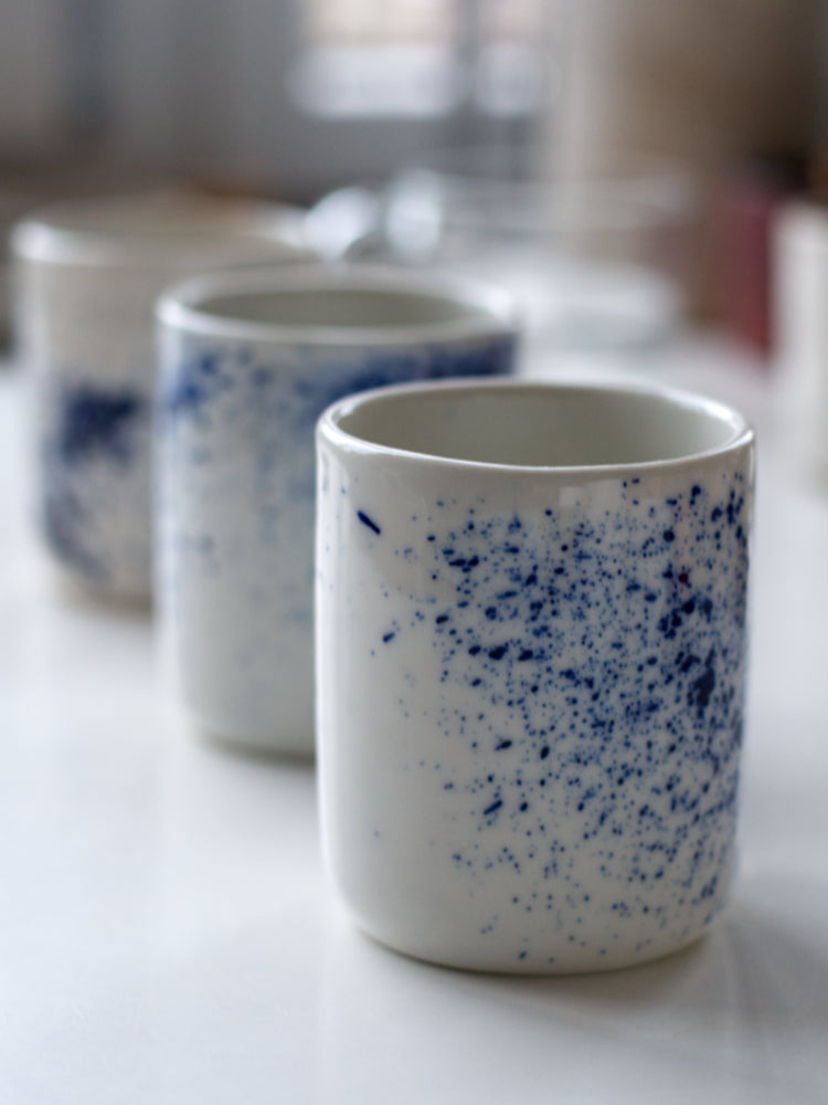 Handgemaakte witte porseleinen kopjes met blauwe spetters op een rijtje op een witte tafel, close gefotografeerd