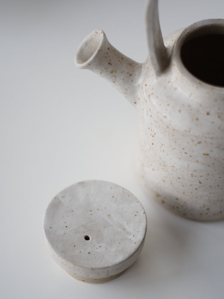 Handgemaakte theepot met whitewashed op boek met tuutje en deksel ernaast gefotografeerd