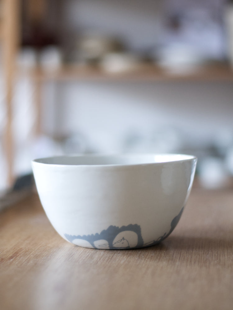 Handgemaakte schaal van wit porselein met een bodem van blauw porselein, grillig patroon. Gefotografeerd op een houten tafel en met vage achtergrond