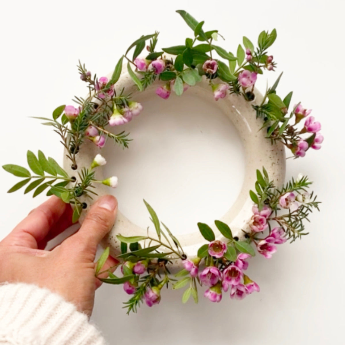 Beige gespikkelde ronde bloemenvaas met roze bloemen, vastgehouden door een hand