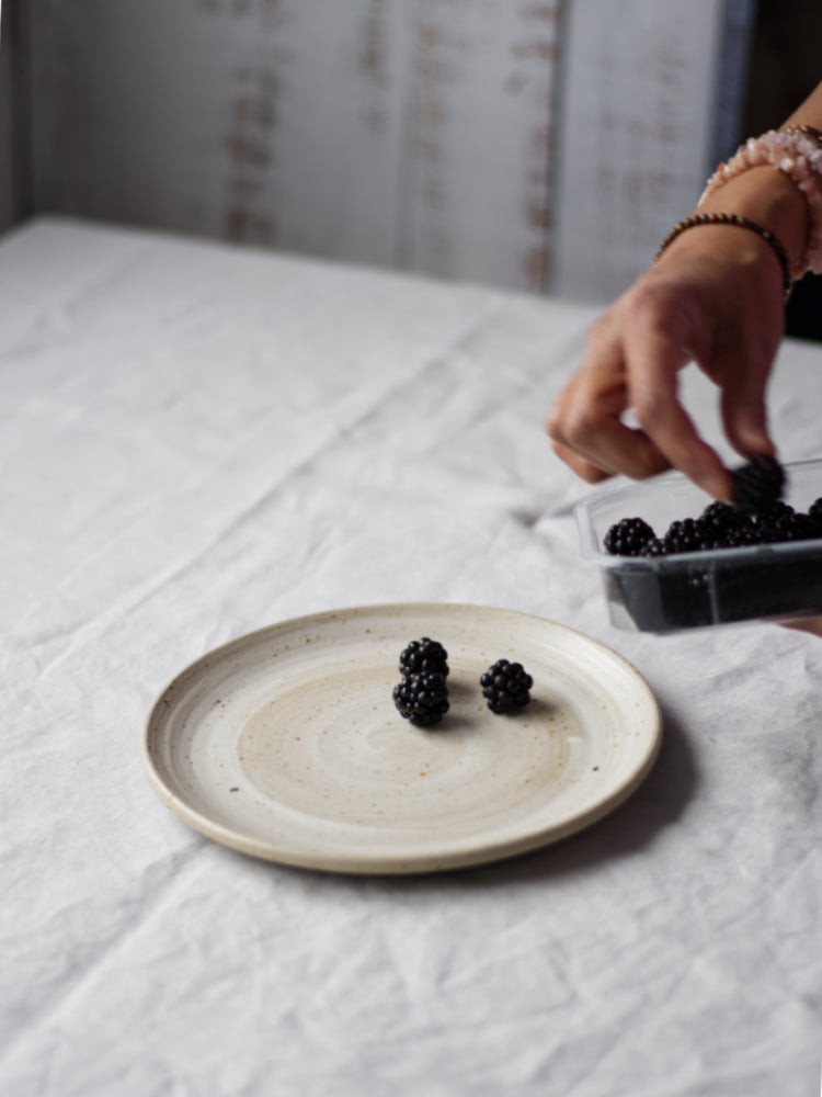 Handgemaakt bord waarop bramen worden gelegd door een hand, op een tafelkleed