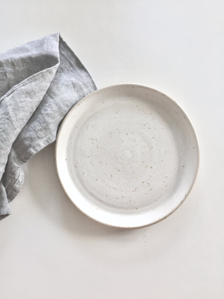 Whitewashed handgemaakt dinerbord met een blauwe theedoek ernaast bovenaanzicht