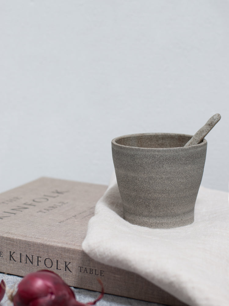 handgemaakt donker kopje met een keramieken lepeltje op een kinfolk boek