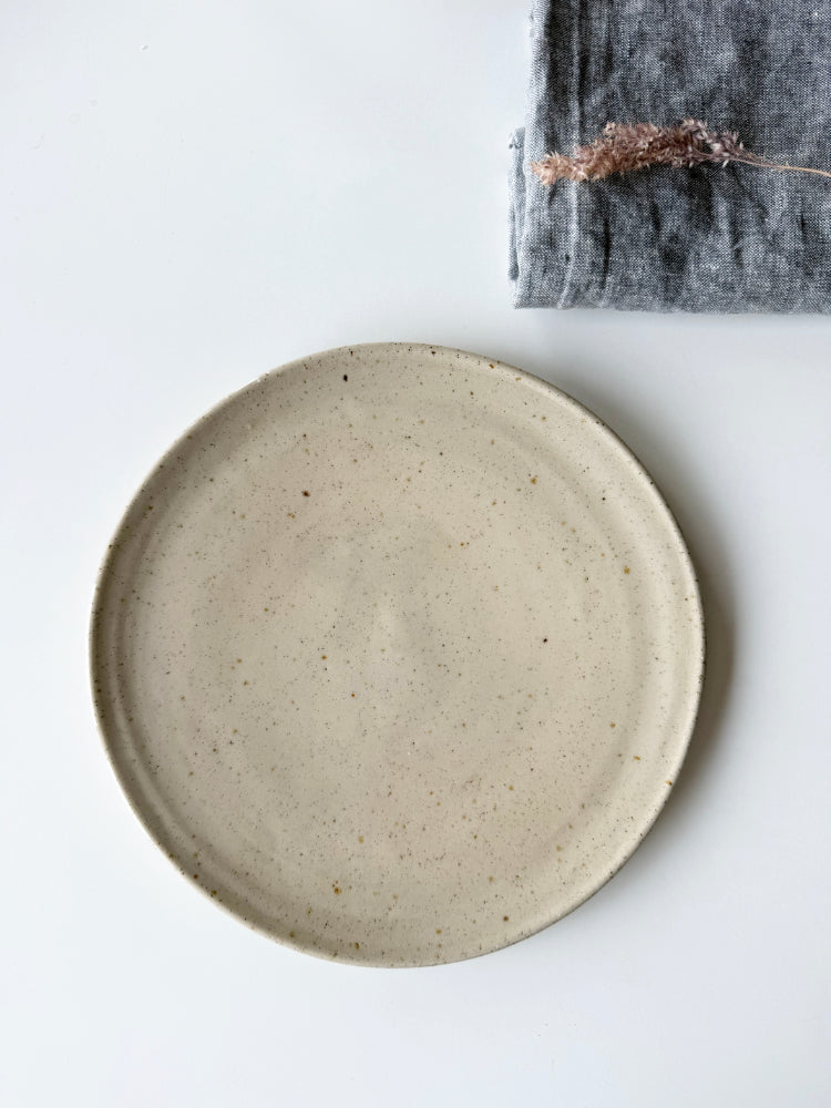 Beige dinerbord op een witte achtergrond met een blauwe theedoek en graspluim erop