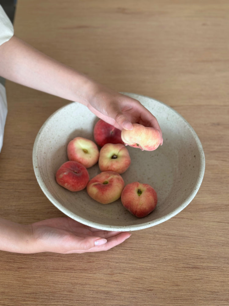 grote handgemaakte keramieken schaal met twee handen met verse perziken op een houten tafel