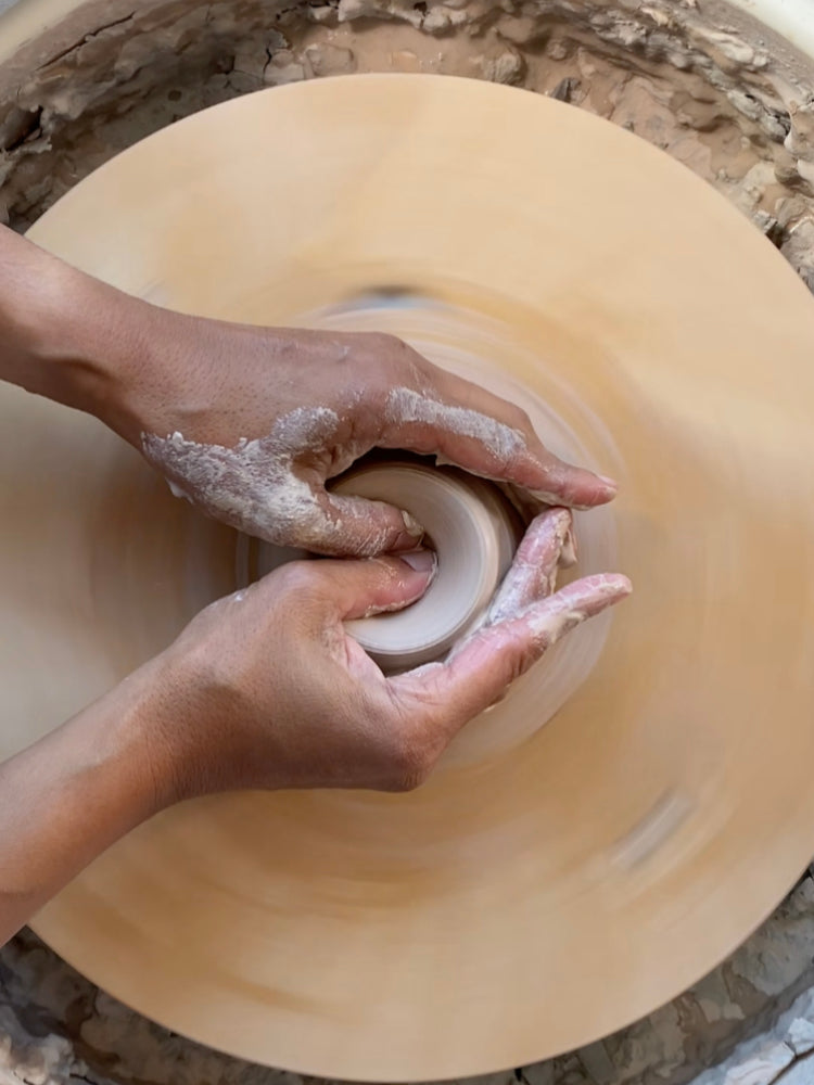 Handen draaiend met klei achter de draaischijf 