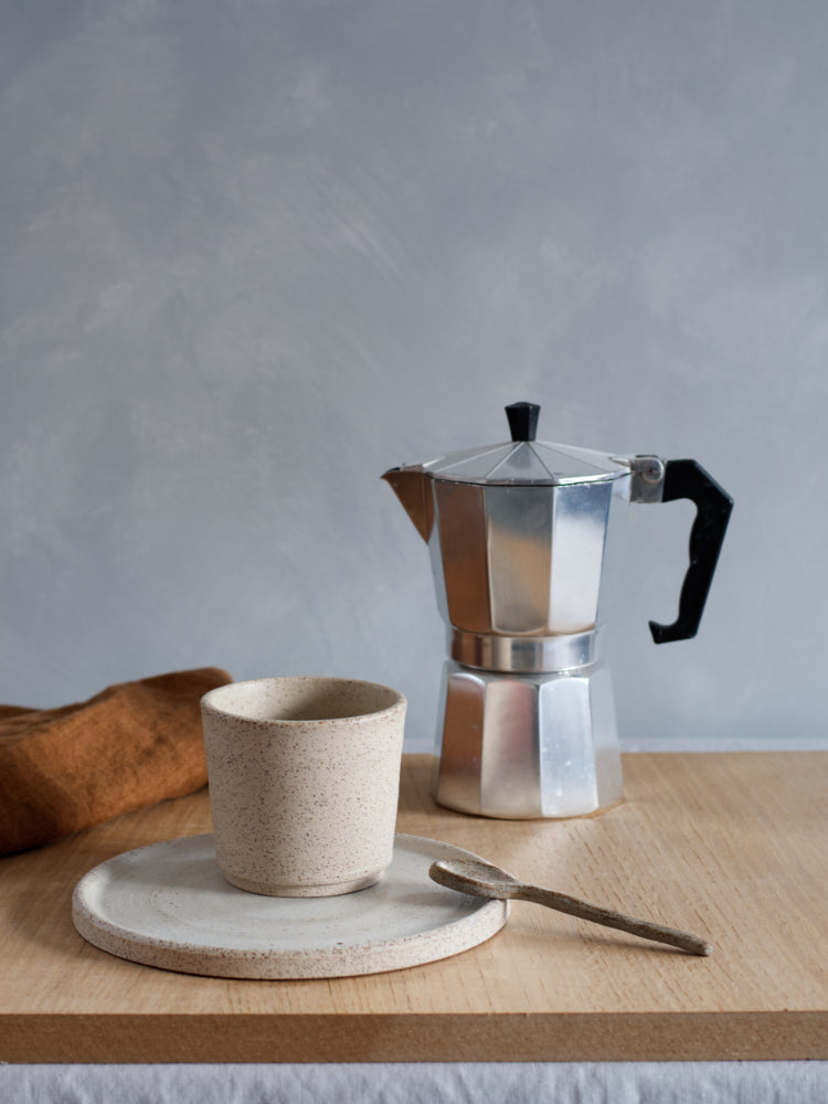 Handgemaakte cakebord met daarop een kopje op een houten plank en daarachter een percolator