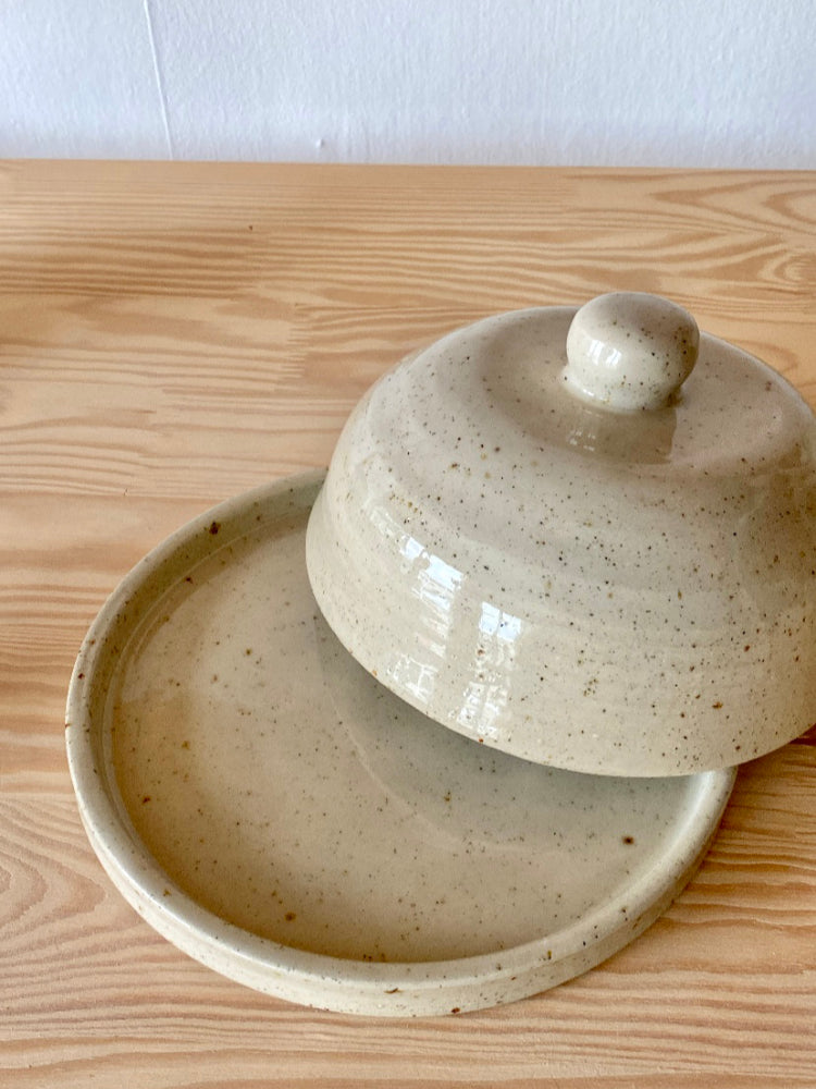 Handgemaakte keramieken stolp met de deksel er half af, gefotografeerd van dichtbij, op een houten ondergrond