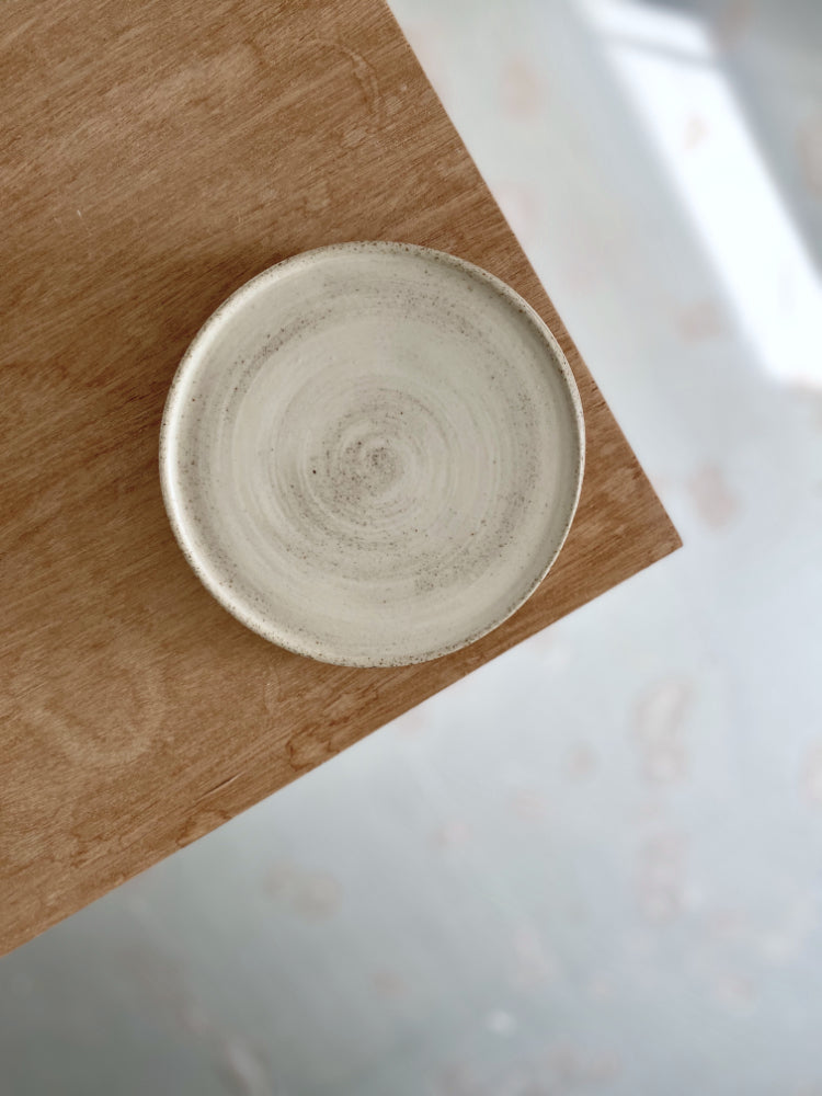 Handgemaakt gespikkeld keramiek cakebord met whitewash en mat glazuur, op de punt van een houten tafel