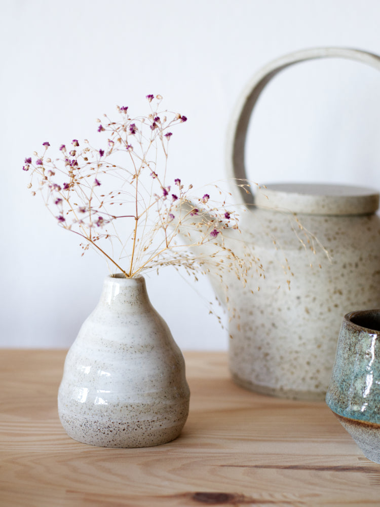 Handgemaakt klein vaasje, gemaakt van gespikkelde klei met licht golvende vorm naast een theepot