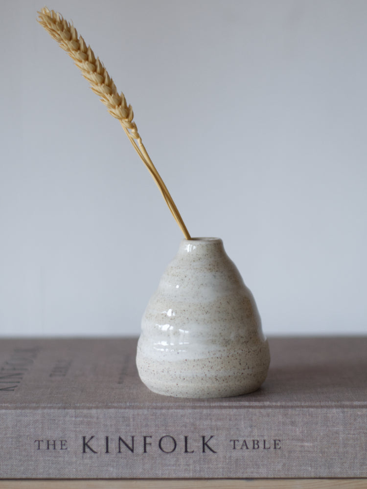 Handgemaakt klein vaasje, gemaakt van gespikkelde klei met licht golvende met een grashalm op een boek gefotografeerd