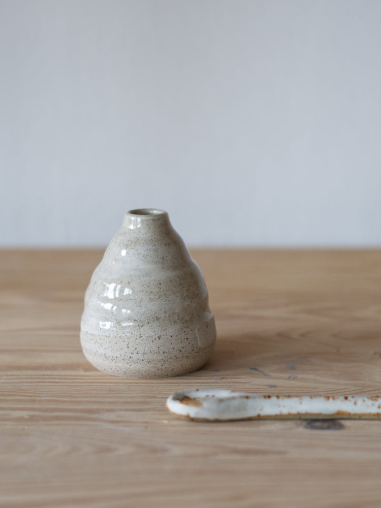 Handgemaakt klein vaasje, gemaakt van gespikkelde klei met licht golvende naast een keramiek lepel