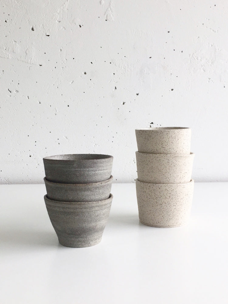 Handgemaakte lichte en donkere  keramieken kopjes gestapeld voor een witte muur