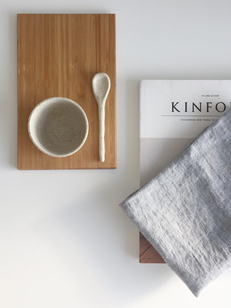 Handgemaakt licht keramieken kopje op een houten plankje met theedoek en Kinfolk boek