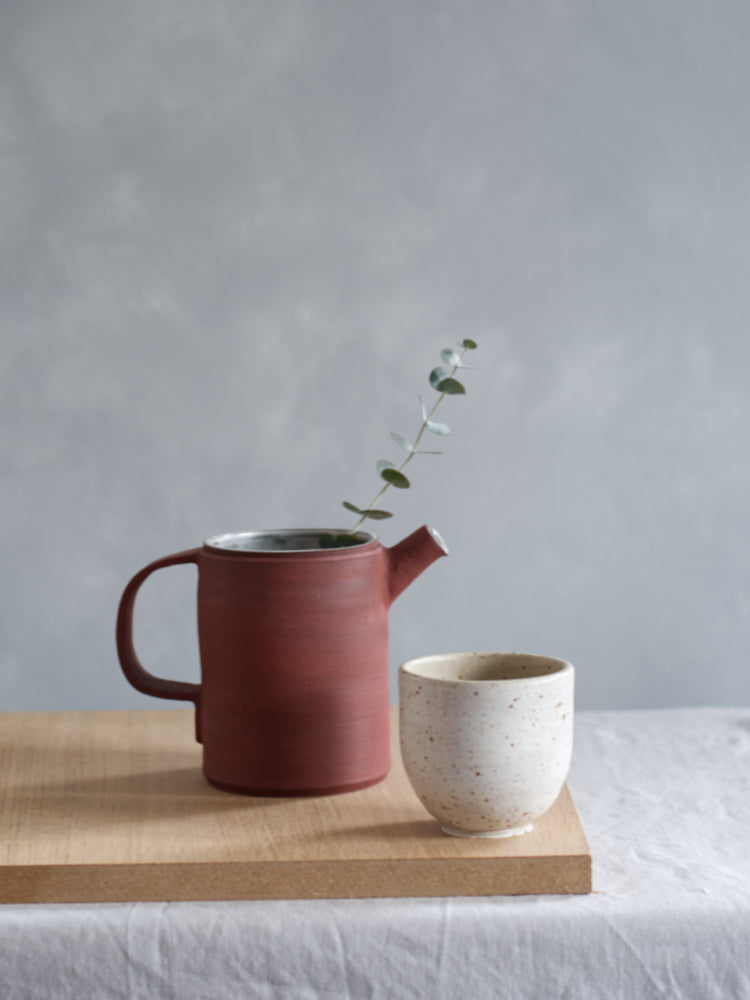 Handgemaakt whitewashed kopje, naast een rode theepot die aan de buitenzijde niet geglazuurd is. 