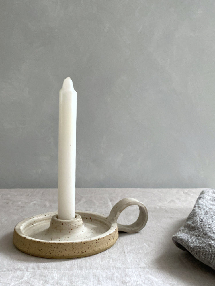 Handgemaakte keramiek kandelaar met handvat, op tafel met een theedoek ernaast.