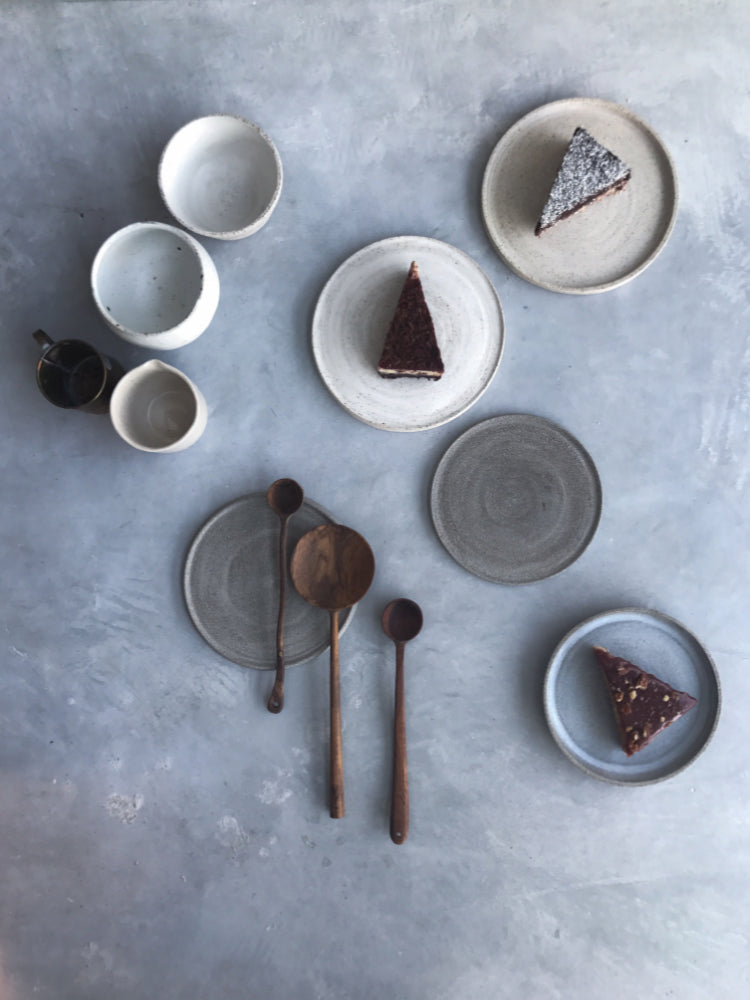 verzameling handgemaakte cakeborden en kommen met cake en houten lepels met een grijsblauwe achtergrond