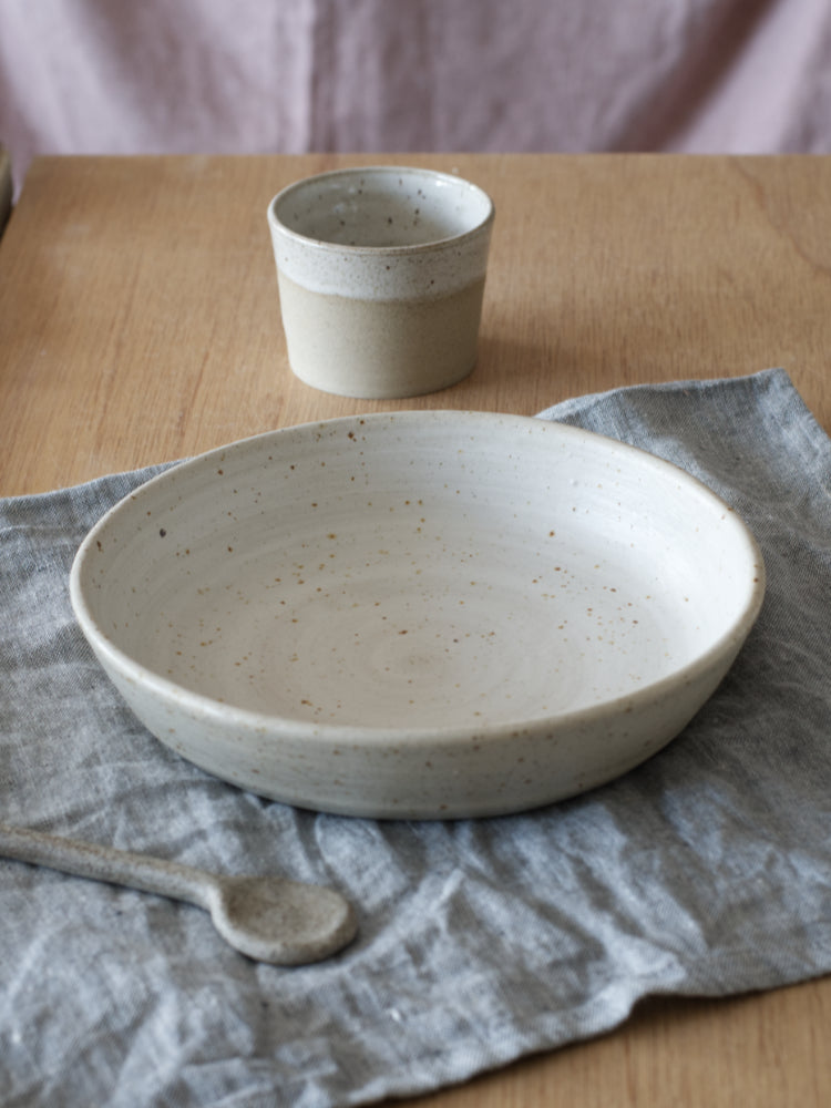 Handgemaakte keramieken whitewashed lage kom met mat glazuur op een grijze theedoek op een houten tafel