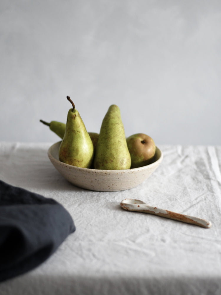 Handgemaakte keramieken kom met peren, keramieken lepel en theedoek op tafelkleed