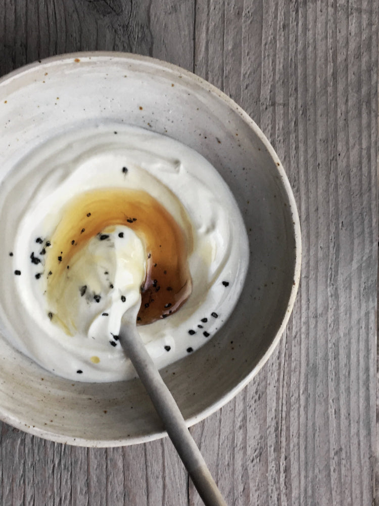 Handgemaakte keramieken kom met yoghurt, honing en lavazout en een keramieken lepel op houten ondergrond