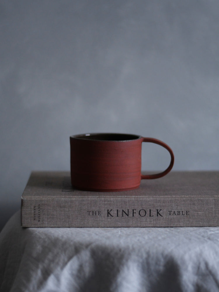 Handgemaakte rode keramieken mok op een kinfolk boek in slow living stijl