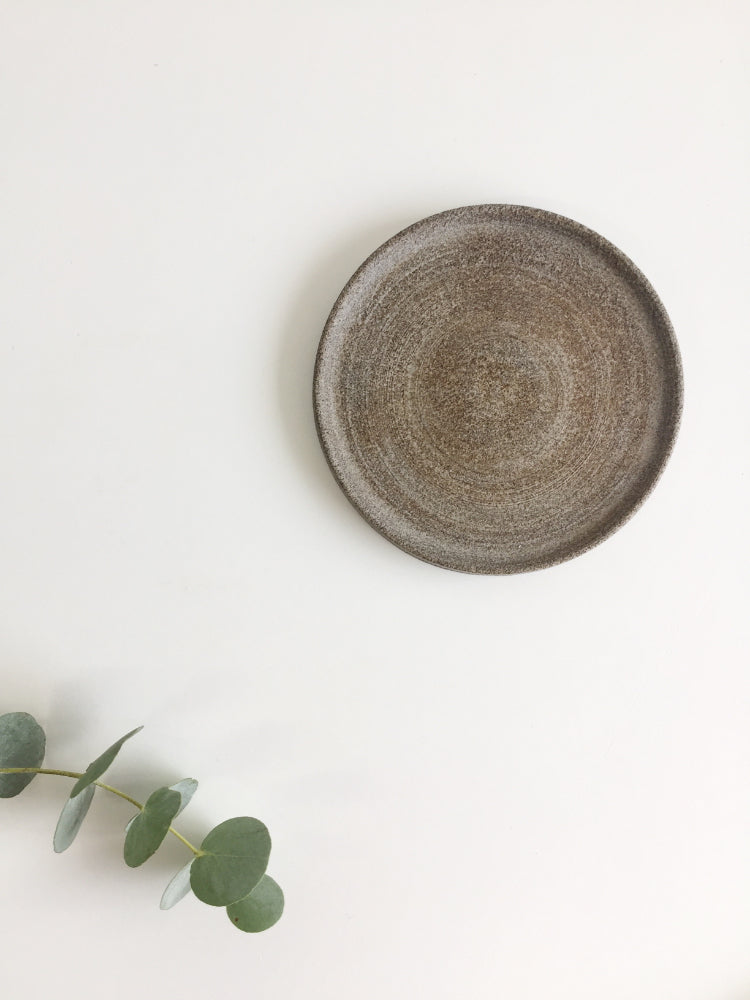 Handgemaakte keramieken schotel op witte achtergrond met groen takje