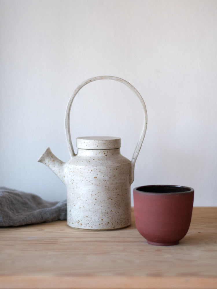 Handgemaakte theepot met whitewashed en naast een kopje van rode klei
