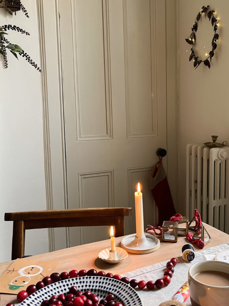 Handgemaakte kandelaar van keramiek op feestelijk gedekte kersttafel met kerstkrans en lampjes