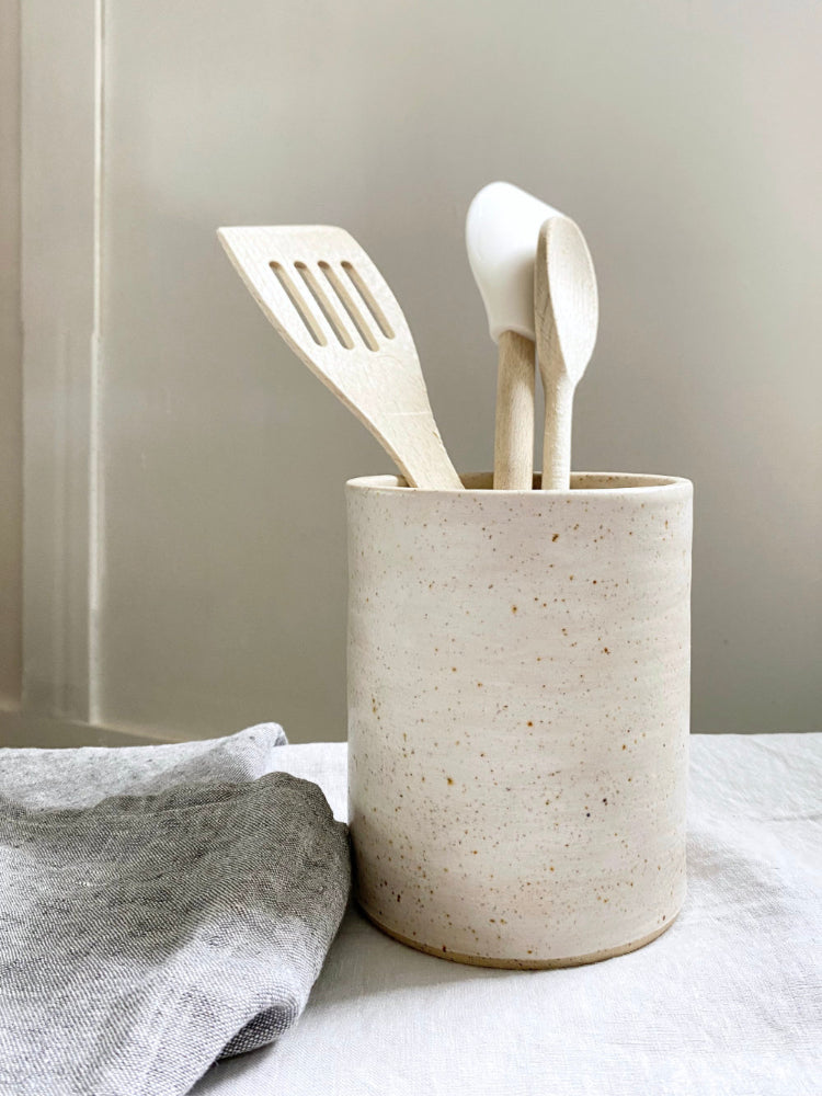 Keukengerei houder van keramiek met spatels erin, naast een theedoek.