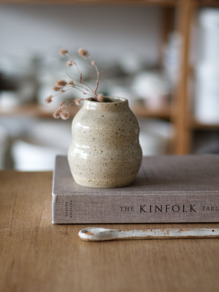 Handgemaakt vaasje gespikkelde klei met glanzend glazuur, op een boek, met een keramiek lepel 