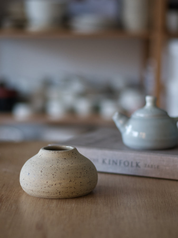 Handgemaakt vaasje gespikkelde klei met ongeglazuurde buitenkant met een boek ernaast, en een theepotje op een houten tafel