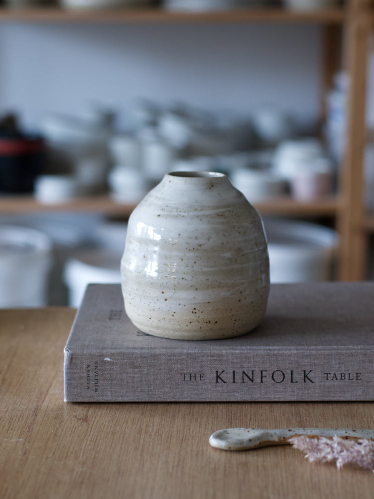Handgemaakt vaasje van gespikkelde klei met wit glanzend glazuur op een boek