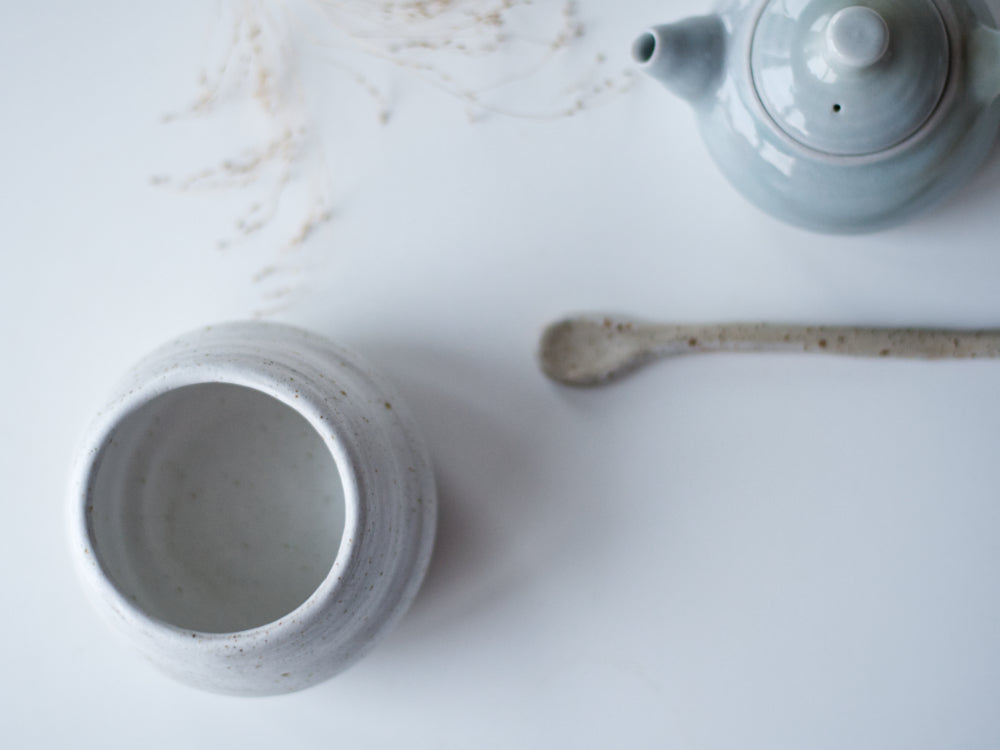 Bovenaanzicht handgemaakt vaasje met mat wit glazuur met een keramiek lepel en een klein blauw theepotje