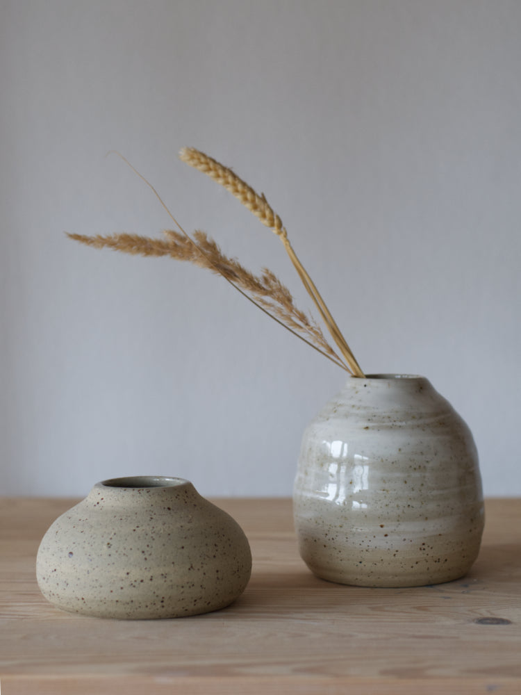 Handgemaakt vaasje van gespikkelde klei met witte slib en glanzend glazuur naast een ongeglazuurd vaasje